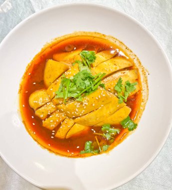 Cilantro ve susam tohumlarıyla süslenmiş baharatlı acı biber sosuna batırılmış, canlı bir dilim haşlanmış tavuk. 