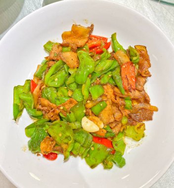 Dilimlenmiş domuz eti, canlı yeşil biber ve sarımsaklı karanfillerle bezenmiş kırmızı biber kızartması.