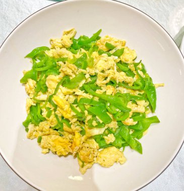 Parlak yeşil dolma biberle karıştırılmış sade ama canlı bir yumurta tabağı, beyaz bir kasede servis ediliyor. 