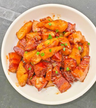 Zengin, koyu bir sosla parlayan ve yeşil soğanla süslenmiş, doyurucu bir domuz eti ve patates tabağı. 