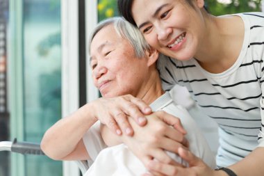 Happy female caregiver hugging old elderly woman from behind with tenderness and love,Asian adult daughter embraced her warmly at home,time spent together,family time,visiting the elderly,relationship