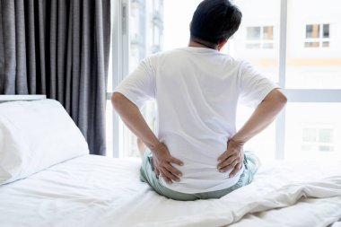 Sırt ağrısı çeken üzgün Asyalı bir adam, kronik bel ağrısı, yatak masajı, bel ağrısı, mutsuz insanlar sabahları rahatsız edici bir yatakta ya da kötü bir duruşda uyuduktan sonra uyanır.