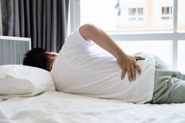 患有背痛 髋关节酸痛 腰痛的紧张的亚洲男人 患有腰痛或急性背痛的不快乐成年人 躺在家里的床垫上 医疗保健 生活方式观念 — 图库照片