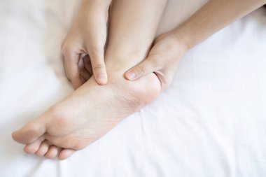 Kızın elleri ayağına masaj yapıyor, ayak bileğinin altında ağrı, düz ayak hastalığı, Tibialis Posterior Disfonksiyon Bozukluğu ya da Plantar Fasciitis sorunu yüzünden ayak ve bilek arasındaki kas iltihabı ve tendon.