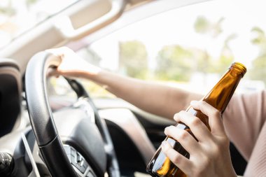 Yaklaş, elinde bira şişesi olan sarhoş bir kadın, motorlu araç kullanırken alkol alan Asyalı bir kadın sürücü, kötü davranışlar, kontrolünü kaybetmek, trafik kazası sorunları, alkollü araç kullanmama konsepti.