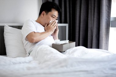 Middle aged man have a stuffy nose,runny nose,blow or wipe one's nose with tissue paper,asian male have a fever and cold or flu,respiratory disease,respiratory tract infection,resting in bed at home clipart
