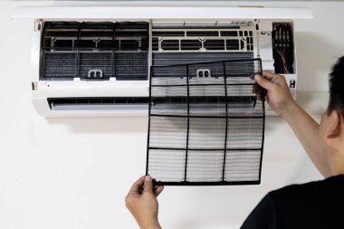 Evde tek başına tıkanan kirleri temizledikten sonra hava filtresi gösteren, havalandırma filtresini değiştirerek ideal performans ve hava kalitesini sağlayan, toz alerjisini önleyen bir adamın elleri