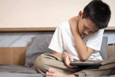 Boyun kası ve omuz ağrısından muzdarip Asyalı bir çocuk, omurga ağrısı, oturma ve sırtını bükme, kötü duruş, cep telefonuyla oyun oynarken uzun süre başını eğme, kötü konum