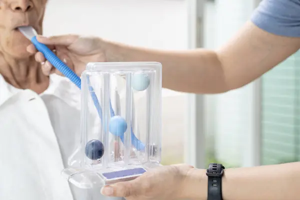 stock image Asian female caregiver holding spirometer,taking care of senior grandmother at nursing home,elderly using spirometer,exercise the lung,help the lung expansion,concept of service,medical,health care