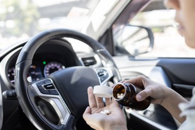 Woman pouring medicine capsule into her palm of hand,taking medication while driving a car,dangers of consuming certain drugs that can cause drowsiness or impair focus,risk of accidents,safety on road clipart