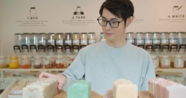 Sıfır atık dükkanından ekolojik organik ürünler alan bir adam. Asyalı erkek plastik markette ekolojik el yapımı sabun tutuyor. Doğal kozmetik ürünleri, cilt bakımı. Sürdürülebilir yaşam tarzı.