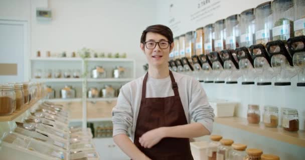 幸せなアジアの男の肖像画環境に優しいお店のオーナー笑顔 プラスチックフリー食料品店の背景にカメラを見て 持続可能な小規模地元のビジネススタートアップはグリーンマーケットに行く 再利用の削減 — ストック動画