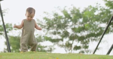Parkta oynayan sevimli, mutlu, küçük çocuk. Yaz tatilinde yeşil çimlerin üzerinde yürüyen tatlı bir kız bebek. Aktif beyaz çocuk güneşli bir bahar gününde açık havada yürümeyi öğreniyor. Yavaş Hareket