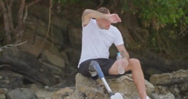 Yapay biyonik bacaklı yorgun sporcu deniz kenarında antrenman yaptıktan sonra oturup dinleniyor. Engelli sporcu koşudan sonra içme suyu molası veriyor ya da antrenman yapıyor..