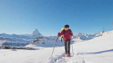 Sırt çantalı Asyalı turist yürüyüşçüsü ünlü Matterhorn arka planına sahip kar ayakkabılarıyla yürüyor. İsviçre Alp Dağları 'na tırmanan maceraperest dağcı. İsviçre seyahat yaşam tarzı kış aktiviteleri.