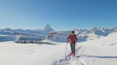 Sırt çantalı Asyalı turist yürüyüşçüsü ünlü Matterhorn arka planına sahip kar ayakkabılarıyla yürüyor. İsviçre Alp Dağları 'na tırmanan maceraperest dağcı. İsviçre seyahat yaşam tarzı kış aktiviteleri.