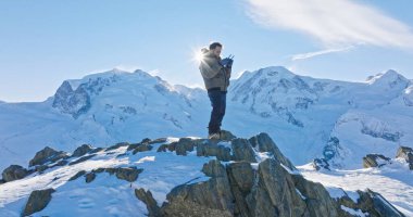Ünlü Gornergrat rasathanesinin tepesinde duran Asyalı genç adamın panoramik manzarası ikonik ünlü Matterhorn gün batımı arka planıyla uzaktan kumandayla çalışıyor. İsviçre Alpleri, İsviçre.