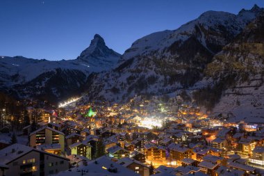 Zermatt Vadisi 'nin ünlü kayak merkezinin panoramik manzarası ve İsviçre' nin İsviçre Alplerinde şafak vakti ikonik Matterhorn zirvesi. Kanton Valais 'teki köy ve kilise kışın karla kaplandı..