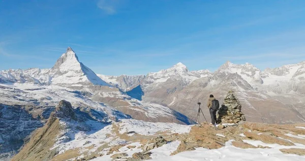 Sırt çantalı genç adamın panoramik manzarası İsviçre 'nin dağ zirvesi manzaralı ve ikonik ünlü manzara olan Matterhorn arka planında fotoğraf çekiyor. Doğa, Seyahat ve Macera konsepti.