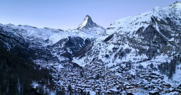 Zermatt Vadisi 'nin ünlü kayak merkezinin panoramik manzarası ve İsviçre' nin İsviçre Alplerinde şafak vakti ikonik Matterhorn zirvesi. Kanton Valais 'teki köy ve kilise kışın karla kaplandı..