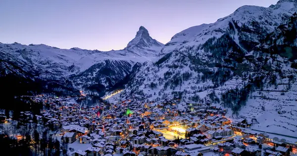 Zermatt Vadisi 'nin ünlü kayak merkezinin panoramik manzarası ve İsviçre' nin İsviçre Alplerinde şafak vakti ikonik Matterhorn zirvesi. Kanton Valais 'teki köy ve kilise kışın karla kaplandı..