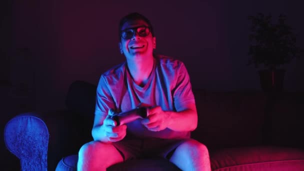 中年人坐在沙发上和控制器玩电子游戏 尼昂闪电电子体育的概念 高质量的4K镜头 — 图库视频影像