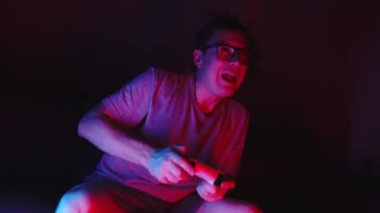 Mid adult man sitting on sofa and playing video games with controller. Neon lightning e-sport concept. High quality 4k footage