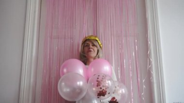 Taçlı altın balonu, püsküllü parti perdesi ve balonları olan olgun bir kadın. Kutlama etkinliği. Yüksek kalite 4k görüntü