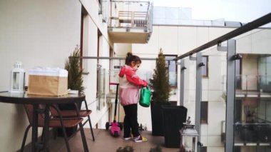 Anaokulu kızı baharda balkonda çiçek suluyor. Balkon şehir bahçesi. Yüksek kalite 4k görüntü