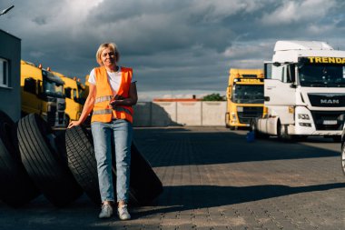 Beyaz, orta yaşlı bir kadın. Otoparkta sarı bir kamyonun önünde. Yüksek kalite fotoğraf