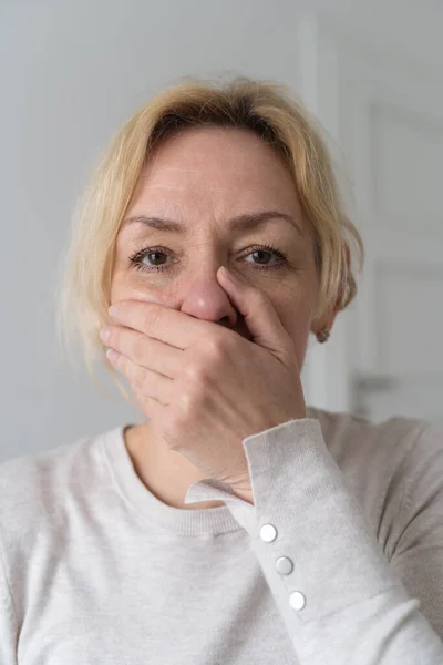 Sad mature woman closes mouth with hand. . High quality photo