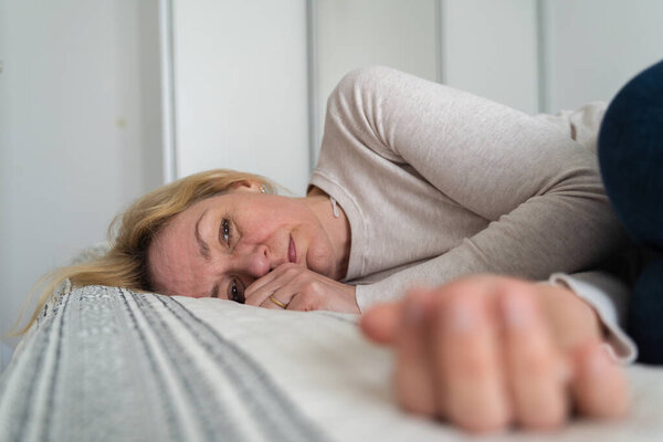 Mature woman curled lying on the bed at home top view. Depression, mental health, abuse problem. High quality photo