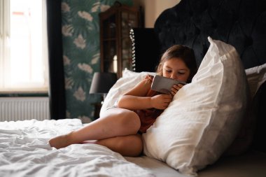 Yatakta cep telefonuyla çizgi film izleyen 5 yaşında bir kız. Kraliyet lüksü. Yüksek kalite fotoğraf