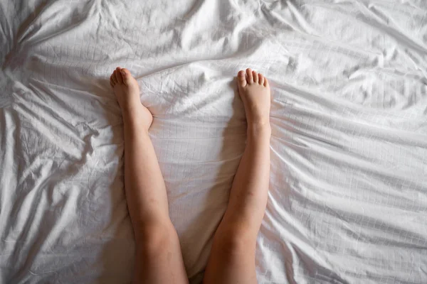 Female legs in white socks in white linens bed, top view Stock