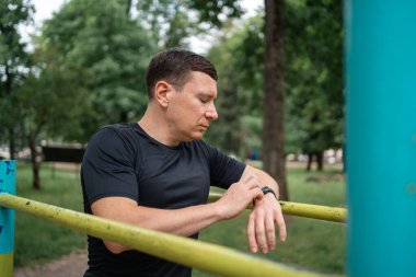 Açık hava barlarında spor yaparken akıllı saati kullanan orta yaşlı bir adam. Yüksek kalite fotoğraf