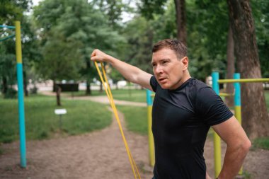 Orta yaşlı bir adam parkta direniş bantlarıyla güç egzersizleri yapıyor. Yüksek kalite fotoğraf