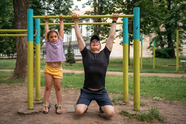 Stock image Father with child girl doing pull-ups on workout outdoor area. Healthy active lifestyle, happy family time. Modern fatherhood concept . High quality photo