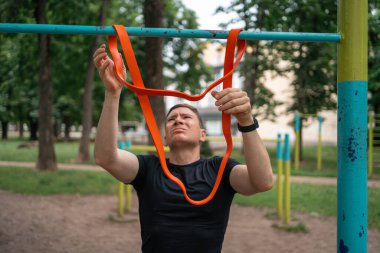 Orta yaşlı bir adam parkta direniş bantlarıyla güç egzersizleri yapıyor. Yüksek kalite fotoğraf