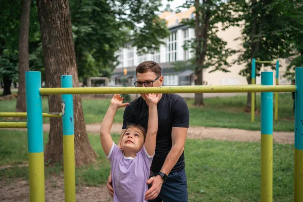 stock image Father with child girl doing pull-ups on workout outdoor area. Healthy active lifestyle, happy family time. Modern fatherhood concept . High quality photo