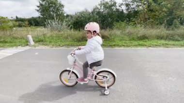 Öğrenme tekerleriyle bisiklet süren koruyucu kasklı bir kız çocuğu. Yüksek kalite 4k görüntü