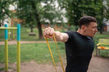 Orta yaşlı bir adam parkta direniş bantlarıyla güç egzersizleri yapıyor. Yüksek kalite fotoğraf