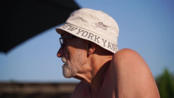 暑い夏の晴れた日にプールの近くでリラックスするひげを持つ80歳の白人男性 ライフスタイルのスタイル 幸せなリアルな感情 高品質の4K映像 — ストック動画