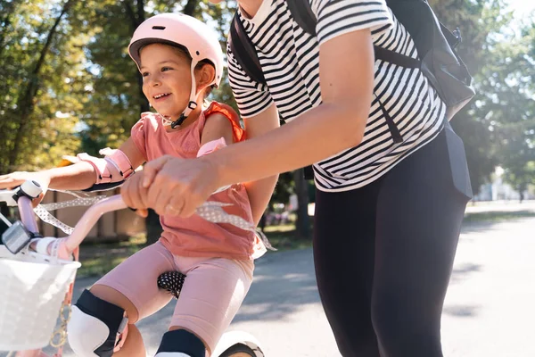 Mother learning child girl to ride a bike in the park in the summer. Happy quality family time together. Empowering, essential physical skills for kids. High quality photo