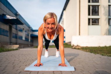 Şehir parkındaki yoga minderinde bitki yetiştiren orta yaşlı müzikal güzel bir kadın. Çekirdek egzersizi. Yüksek kalite fotoğraf