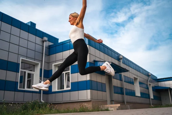 Cauacsian middle age muscular build woman jumping outdoors during her workout. Healthy active lifestyle in urban area. High quality photo