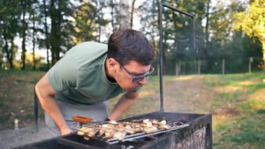 Orta yaşlı beyaz bir adam ızgara şampiyonları pişirirken kömürlere hava üflüyor. Açık havada mangal partisi, basit, lezzetli bir yemek. Yüksek kalite 4k görüntü