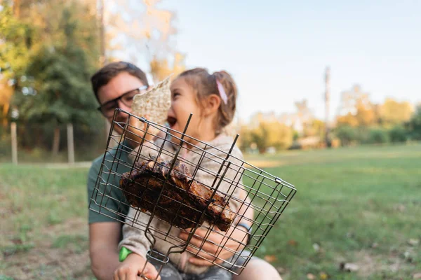Child girl with father portrait outdoors with grill bbq net with beef steak meat. Happy family weekend at the backyard party. . High quality photo