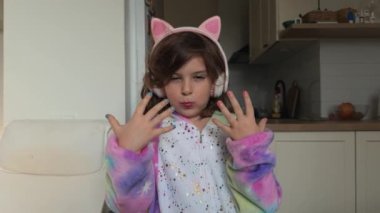 Waist up video of a child girl 5 years old with kids makeup and nails polish, kitten pink headphones and rainbow unicorn kigurumi at home. High quality 4k footage