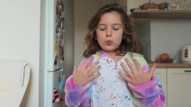 Waist up video of a child girl 5 years old with kids makeup and nails polish and rainbow unicorn kigurumi at home, funny listening to music. High quality 4k footage