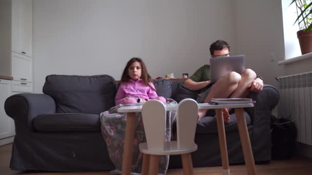 子供の少女 ソファーでビデオゲームをプレイしながら 父親はラップトップで働いています 高品質の4K映像 — ストック動画